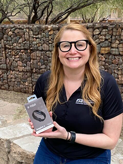 HIP contest winner Kristen Peña holds a boxed Fitbit in an outdoor setting.