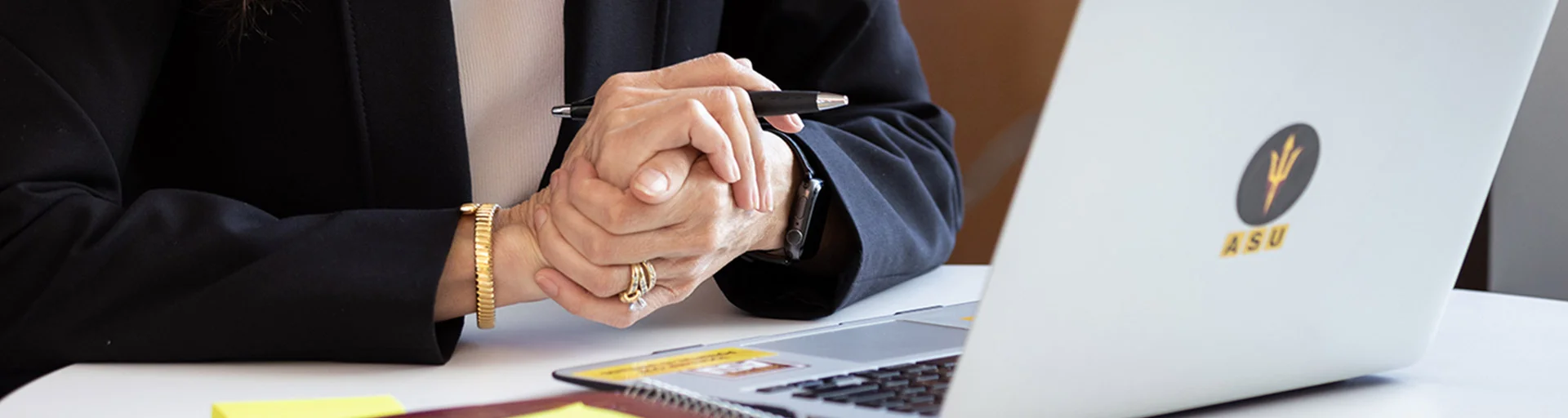 Image of hands holding a pen, papers and laptop on the table. 